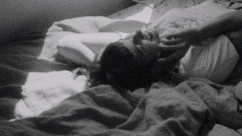 Black and white still of a woman laying on a bed talking on a phone