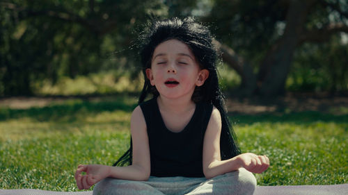 A child wearing a long black wig sits in a yoga pose