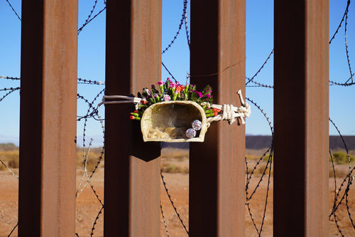 Ceramic figure holding flowers, tied to the US/Mexico border fence