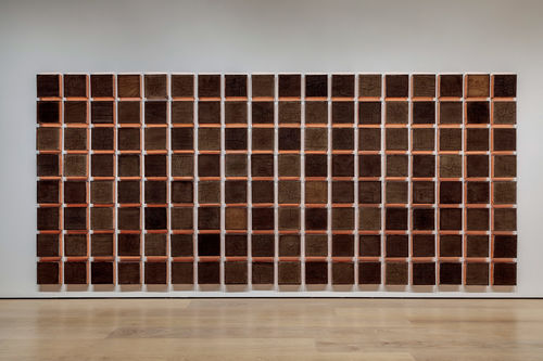 A massive, wall-sized grid of square etchings on "canvases" made of compacted dirt