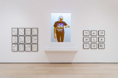 View of a gallery wall with framed drawings and an projected photo of Pippa Garner