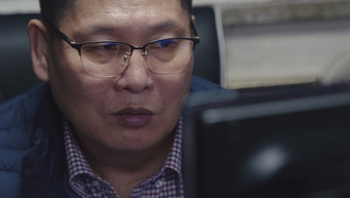 A Korean man wearing glasses sits at a computer monitor