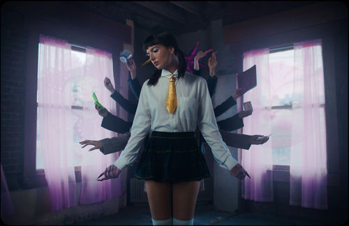 Film still of a video showing a White woman in a schoolgirl uniform with multiple arms haloing her