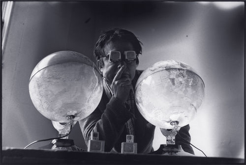 Nam June Paik wearing glasses and resting between two globes