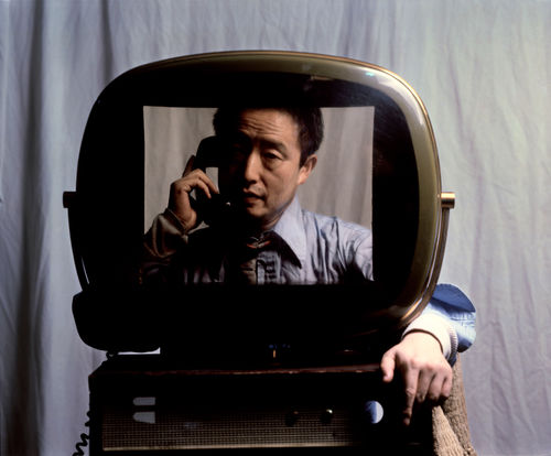 Nam June Paik speaking on a phone handset, seen through an old TV monitor