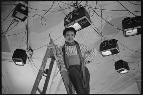 Nam June Paik standing on a ladder