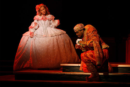 A hunchbacked man kneels in front of a woman in a huge, Victorian dress 
