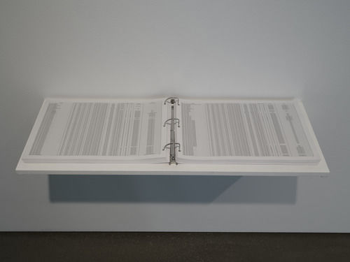 An open white binder containing several pages of video metadata , installed on a wall-mounted shelf