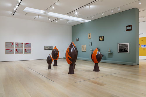 Installation image showing wall-mounted artworks and orange & black sculptures on the floor