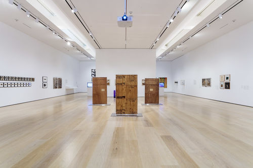Installation image showing wall-mounted artworks and sculptures made of wood on the floor