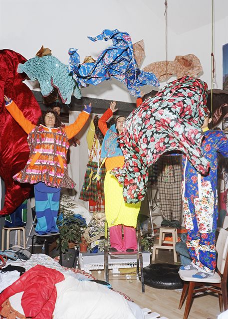 A group of people wearing colorful, abstract patterned textiles and standing on chairs