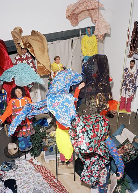 A group of people wearing colorful, abstract patterned textiles and standing on chairs