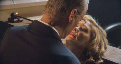A man leans over a woman on the witness stand, as if about to kiss her. A tear appears on the woman's cheek.