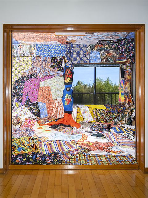 Image depicting numerous pieces of colorful, abstract textiles covering a large room from floor to ceiling