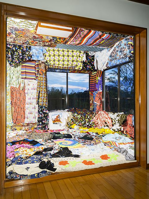 Image depicting numerous pieces of colorful, abstract textiles covering a large room from floor to ceiling