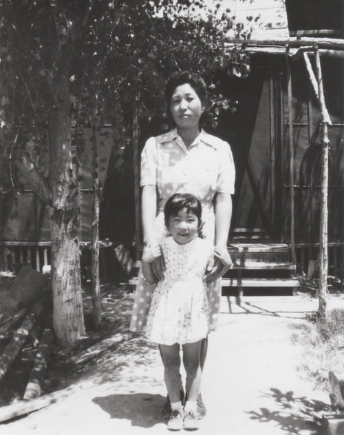 Black and whit the photo of a mother standing, holding her young daughter in front of her