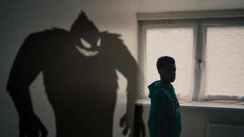 A boy stands in a room with a scary shadow behind him