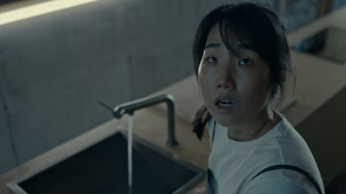 A woman standing at a sink looks up, mouth agape