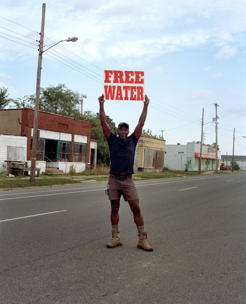 A Black man holds a "Free Water" sign above his head
