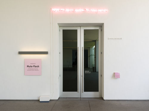Exterior image of Vault gallery with a pink exhibition title card and pink neon sign