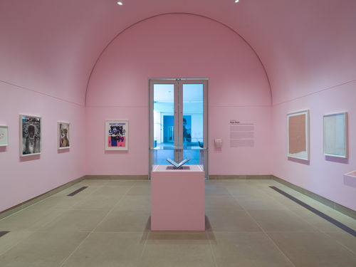 Installation view of framed works on paper installed on wall and in vitrines, the Vault gallery walls painted pink