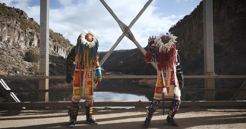 Two figures in colorful costumes standing on a bridge