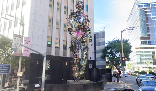 Rendering of a towering digital sculpture of a figure standing on an outdoor plinth
