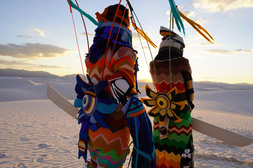 Two figures in colorful costumes stand in a desert