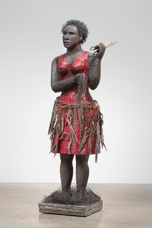 Sculpture of a woman holding a pair of scissors, having recently cut her hair, which lays at her feet