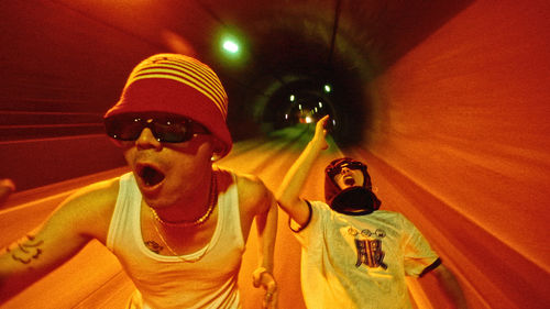 Two men in sunglasses run through a tunnel