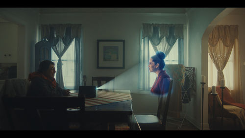 A woman sitting at a table interacts with a woman being projected in front of her