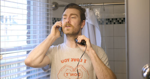 A man talks on a cell phone while clipping his beard