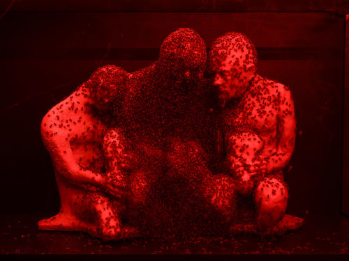 Sculpture in the shape of three huddled figured, covered in bees