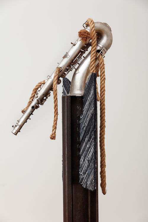Assemblage featuring a saxophone perched atop a wood beam