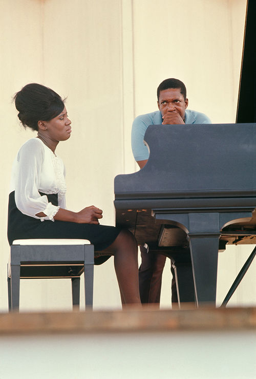 Alice Coltrane sits at a piano with her husband John Coltrane