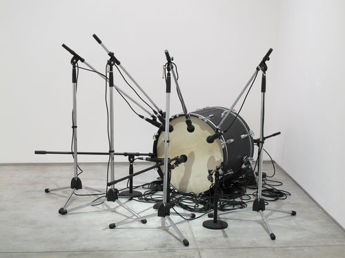 A bass drum sits on the floor surrounded by an array of microphones