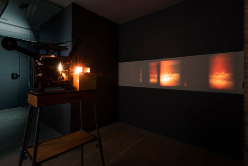 Image of a gallery with a film projector showing film of a cloudy sky