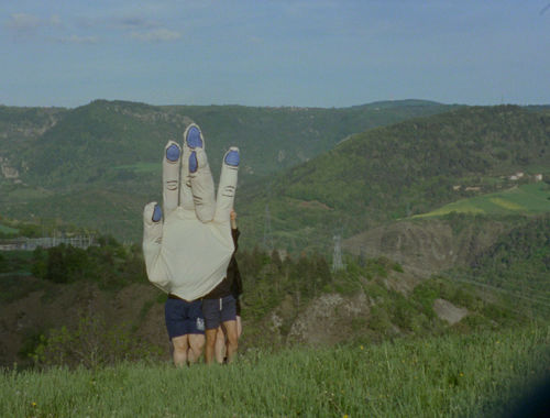 Multiple people wearing a large hand costume in a green field