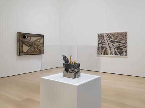 installation image with two framed works on a wall and a sculpture inside a vitrine