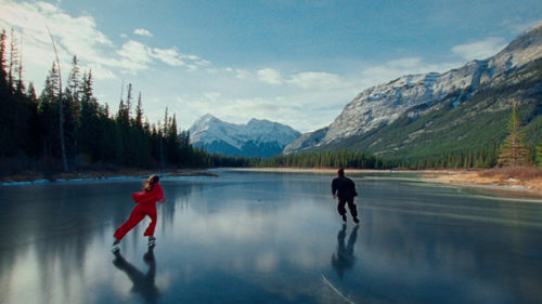 Two figures skate on a frozen lake