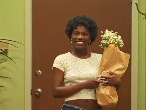 A smiling woman holds a brown paper bag with flowers sticking out of it