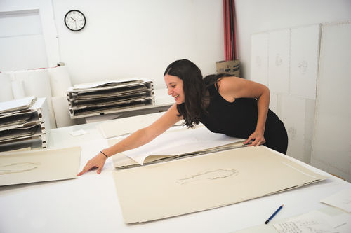 Analia Saban leans over a table to point at a print