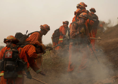 A line of inmates dressed in orange firefighting gear, digging a trench