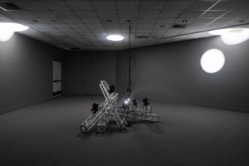 A metal installation at the center, with light and shadow in the background.