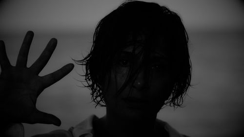 A figure in shadows holds their hand up