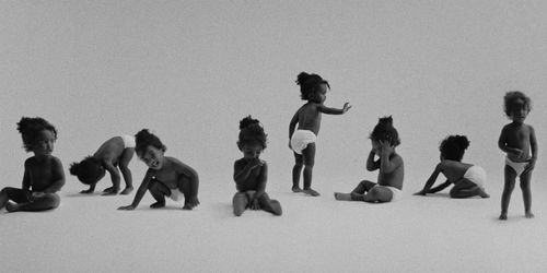 Eight babies in diapers crawling, standing, and sitting against a white background