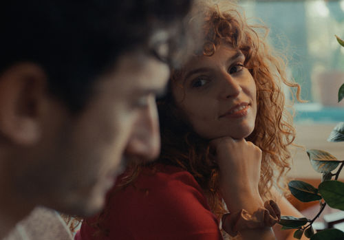 A figure in a red top looks at the profile of another figure