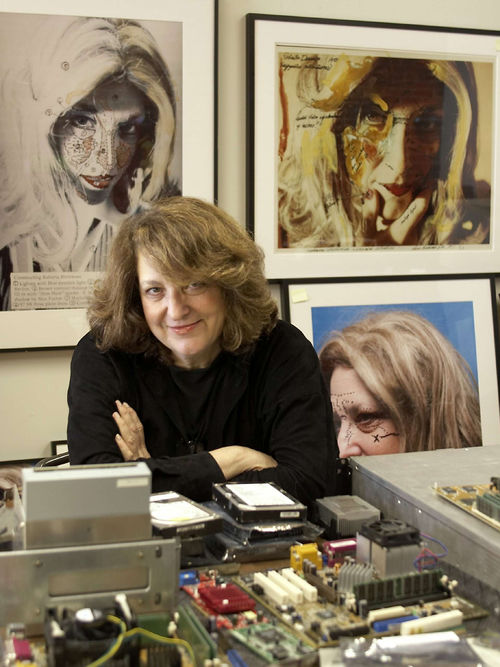 Lynn Hershman Leeson in her office with framed artwork on the walls behind her