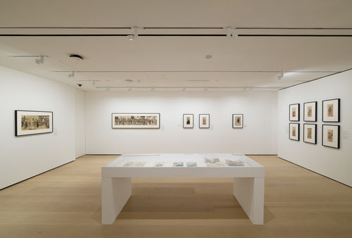 Gallery with framed works on paper installed on walls and inside a vitrine
