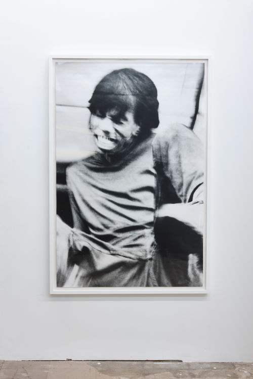 A figure with long bangs smiles wide, the image blurred as if from motion